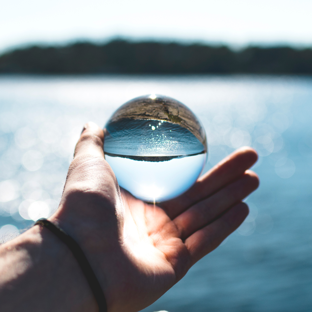 Image of hand holding a transparent sphere with image of lake behind. Credit Canva Images by Sindre Fs from Pexels